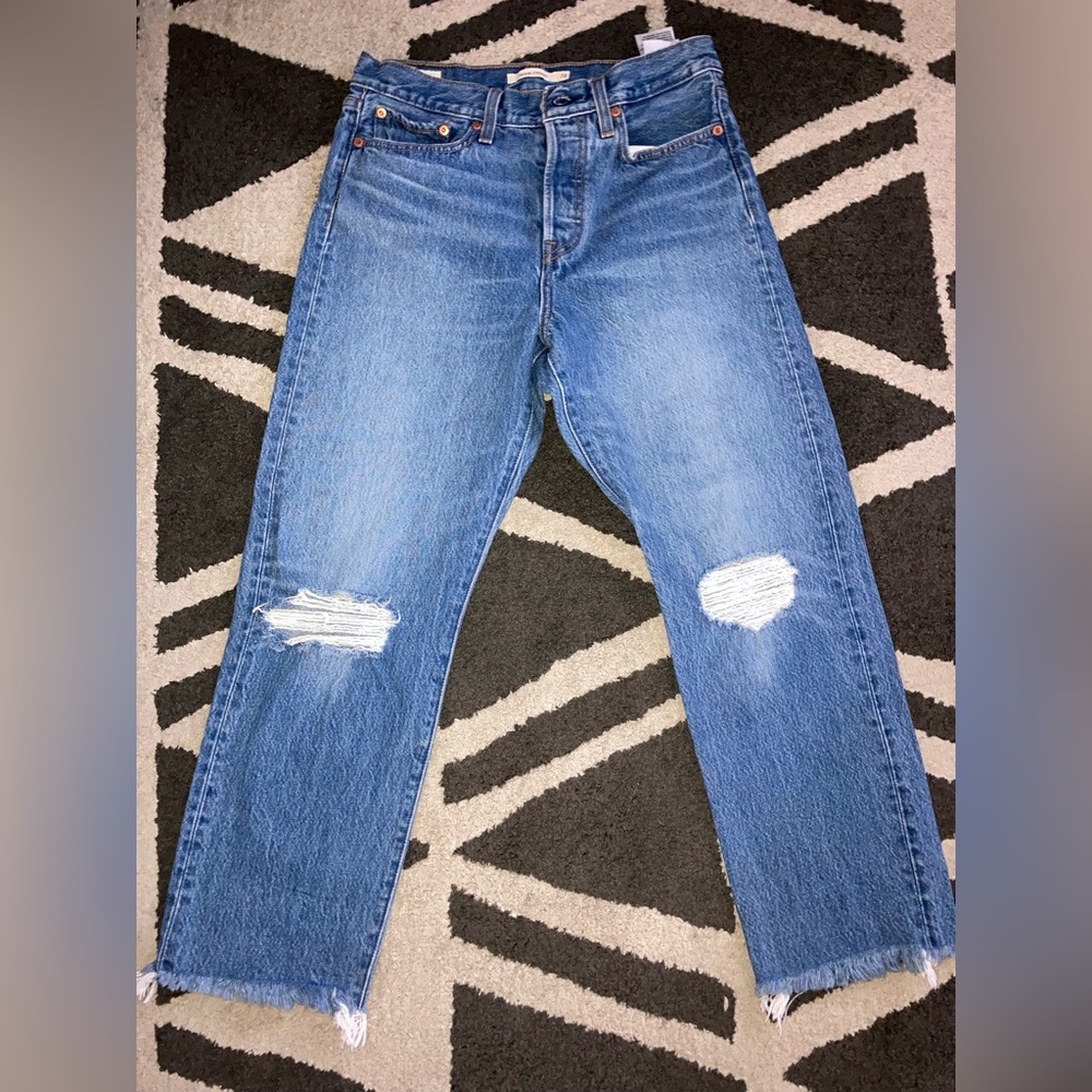 Blue light wash Levi’s straight jeans, button up, distressed hem at bottom.